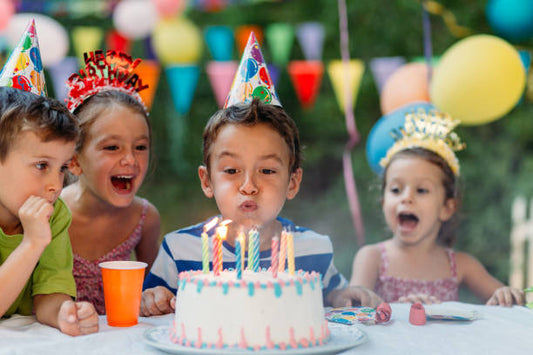 Children celebrating a birthday party with a candle-lit cake and colourful party decorations
